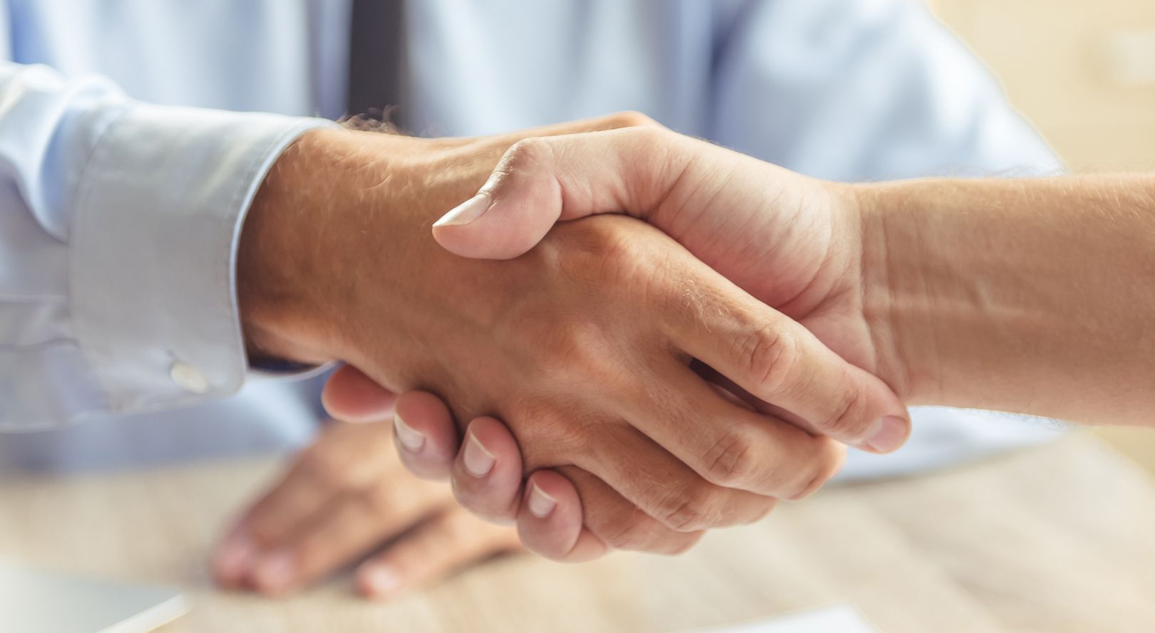Zwei Hände geben sich über einem Tisch die Hand