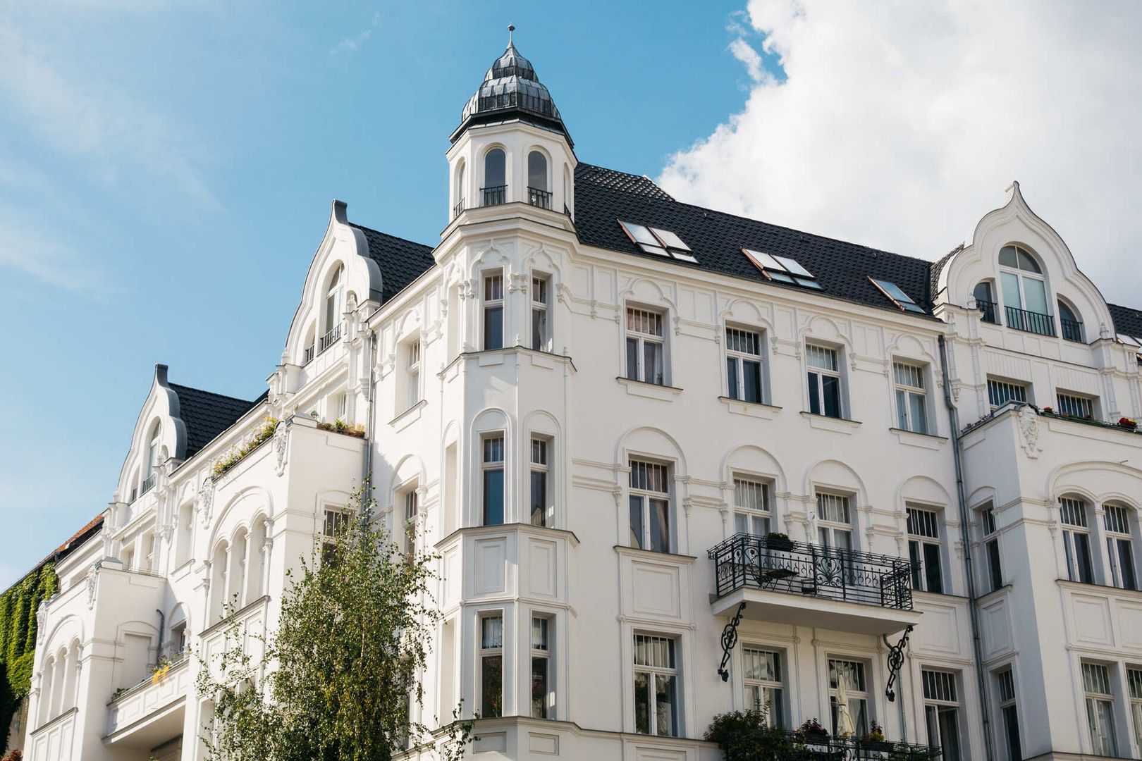 Ein weißes Altbauhaus mit einem Turm vor blauem Himmel im Hintergrund